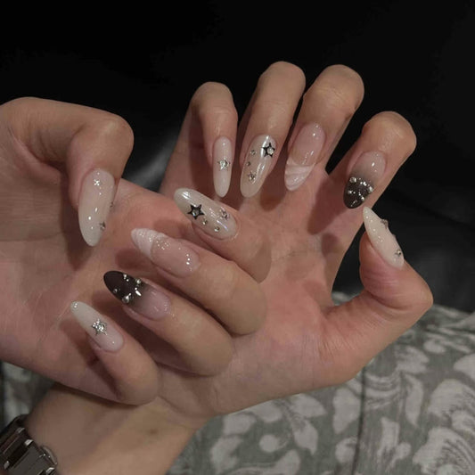 Bold almond-shaped nails featuring metallic star studs, black-to-nude gradients & rock-chic aesthetic for statement looks