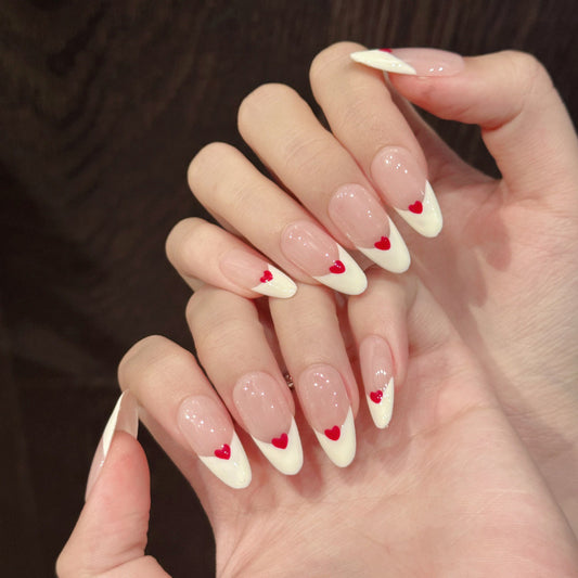 Elegant almond-shaped nails featuring white French tips with charming red heart details - perfect for romantic occasions