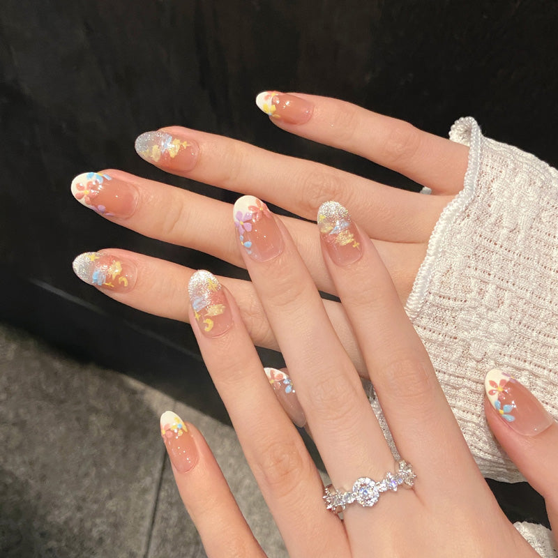 Enchanting oval-shaped short nails featuring delicate hand-painted flowers in pink, blue & yellow with nude base
