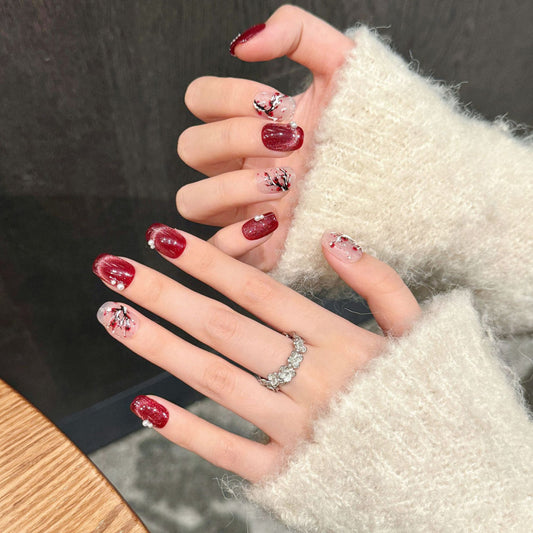 Enchanting squoval-shaped short nails featuring hand-painted cherry blossoms, rich red glitter & romantic pearl details
