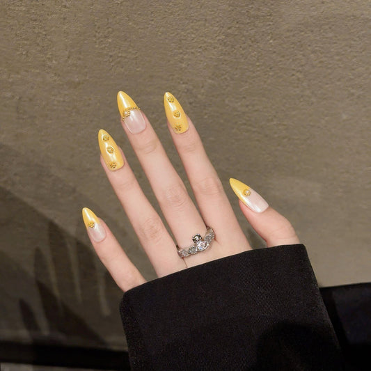 Exquisite almond-shaped nails featuring rich golden tones, chain embellishments & crystal accents for ultimate glamour