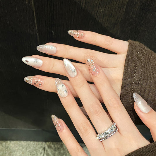 Stunning almond-shaped nails featuring enchanting star patterns, warm metallic tones & sophisticated nude finish