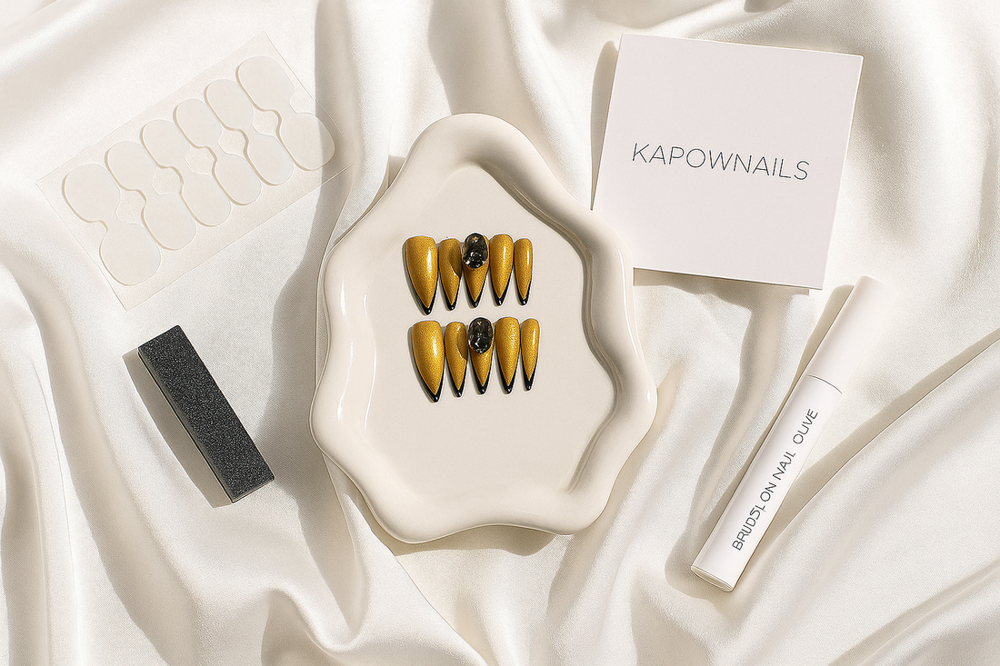 Elegant flat lay of glossy press-on nails, nail glue, buffer, and adhesive tabs arranged on a white silk cloth with soft daylight and shadows. Include a minimal KAPOWNAILS logo card in the corner. Feminine, premium, modern aesthetic.