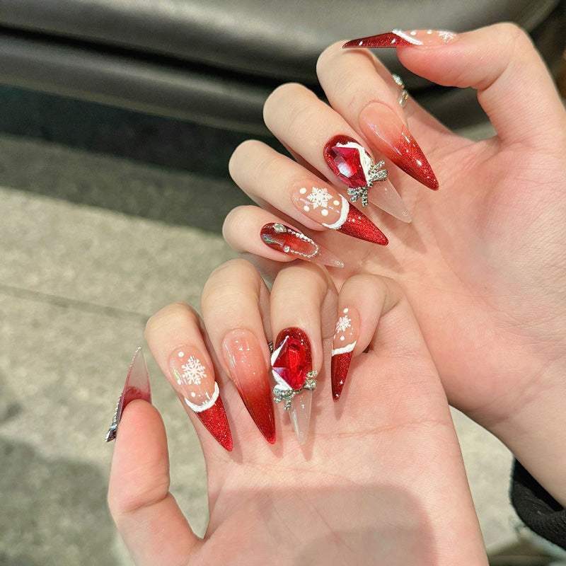 Elegant stiletto long press-on nails with red glitter, snowflakes, ruby gem & silver bow - perfect for festive red elegance & Christmas glamour