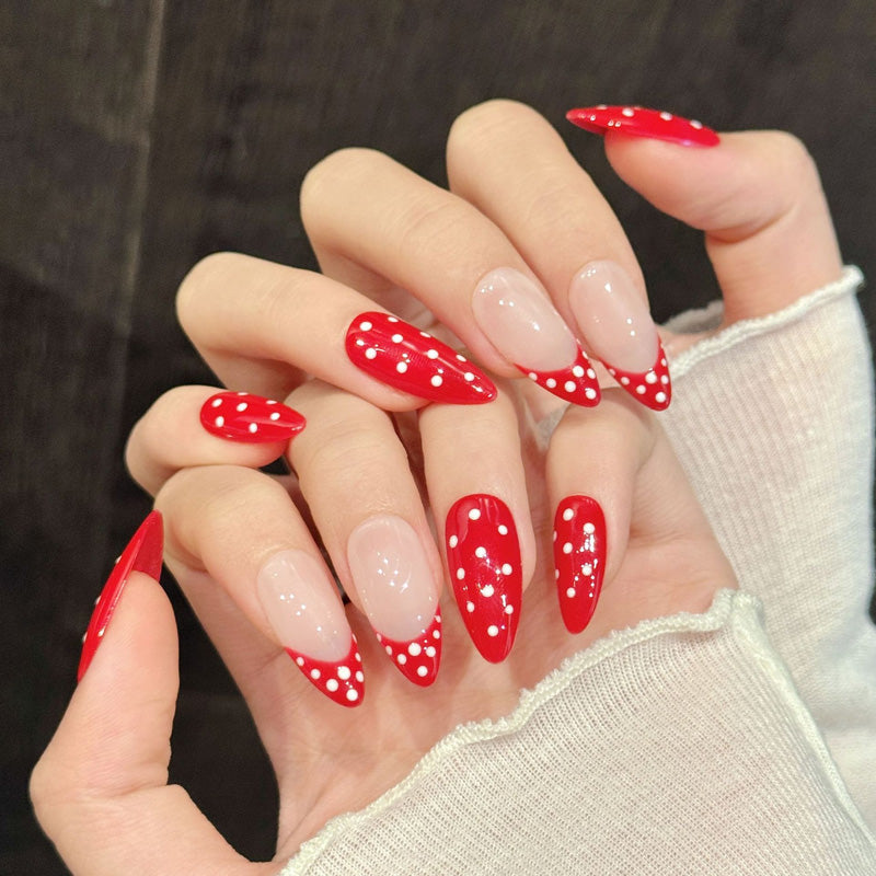 Handcrafted almond nails in bold cherry red with playful white polka dots & elegant nude accents - perfect for holiday celebrations