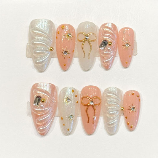 Whimsical handmade almond nails with peach tones, gold bows & celestial charms - Dreamy elegance - Applies in 15 minutes